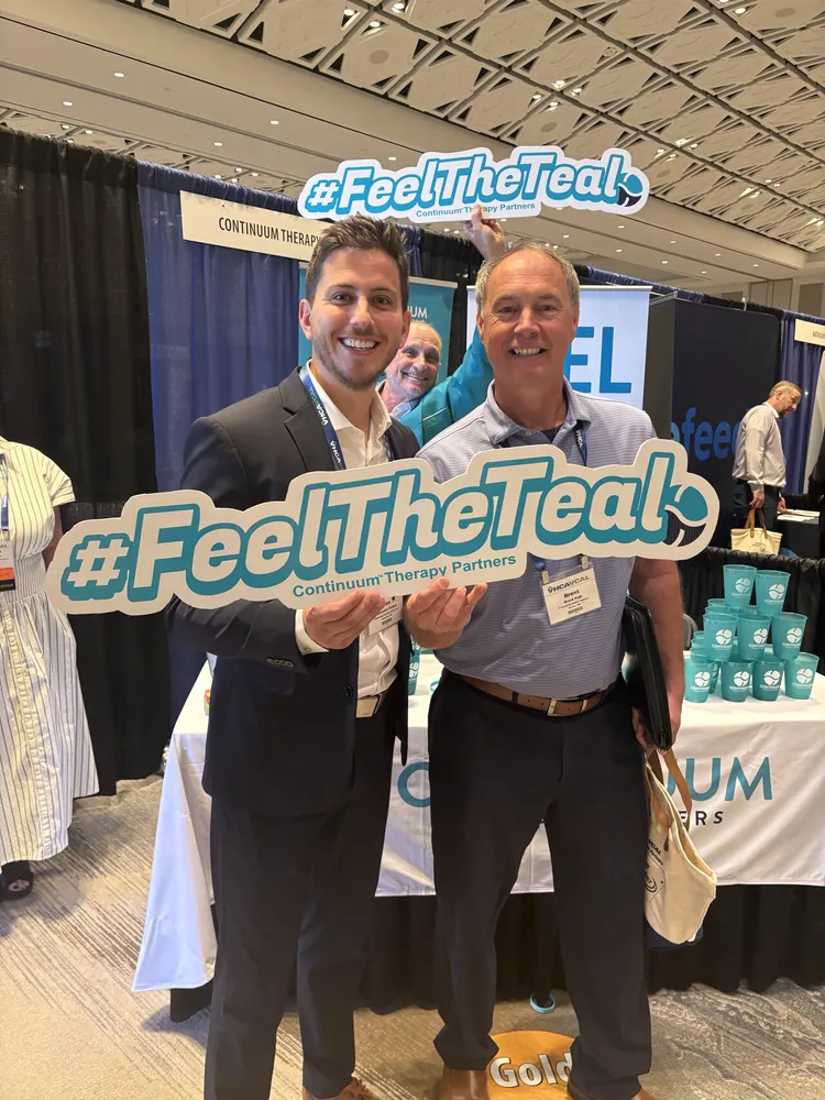 Two attendees holding the #FeelTheTeal sign at the Continuum booth