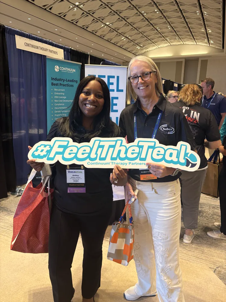 Two conference attendees holding the #FeelTheTeal sign
