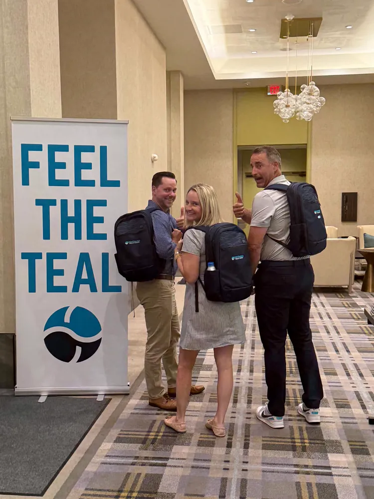 Continuum team members with new backpacks beside a Feel the Teal banner