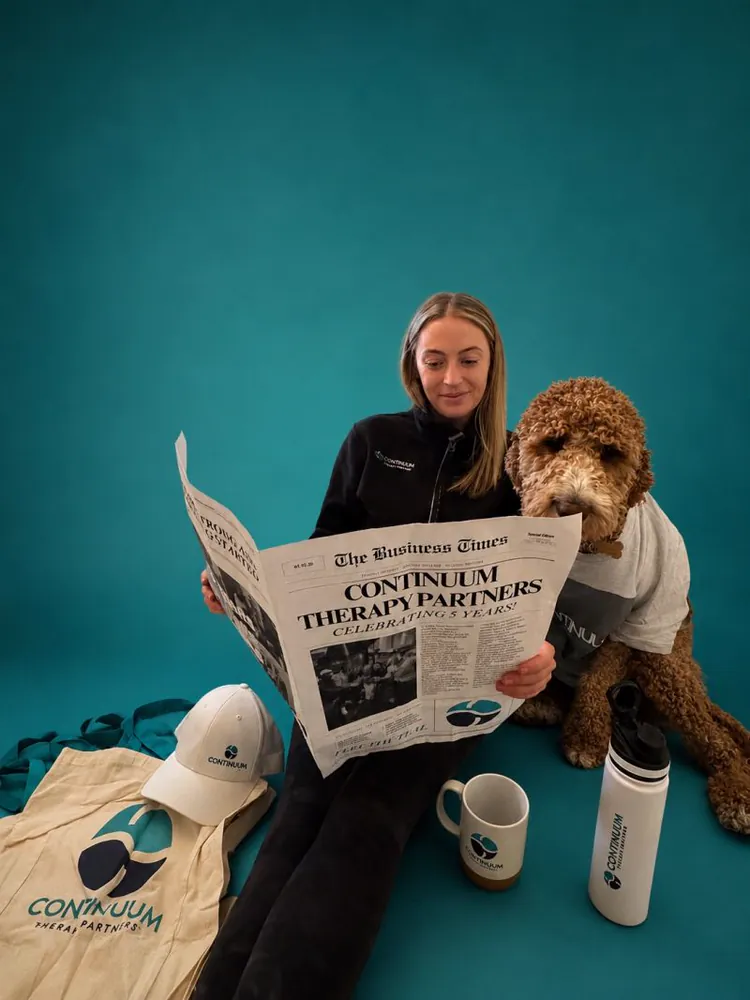 A Continuum team member and a dog reading the five-year anniversary newspaper